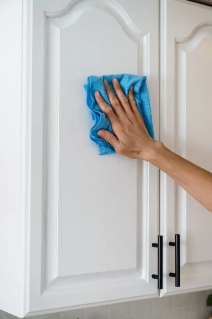 who-we-are Person in protective gear disinfecting bathroom sink with spray bottle.